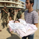 Nahr el Bared, 11 October 2007. A Palestinian refugee carries his new born child past Lebanee soldiers returning home to the bombed-out refugee camp.