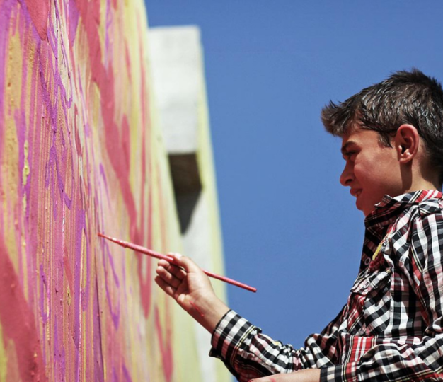 A Syrian child drawing on a wall in colors