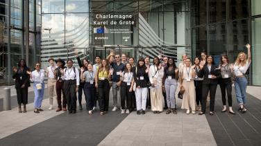 A large group of young people pose and smile outside an EU official building