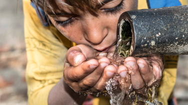 a boy drinking water from a tap
