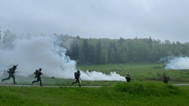 Soliders in training move across a battlefield with smoke screens