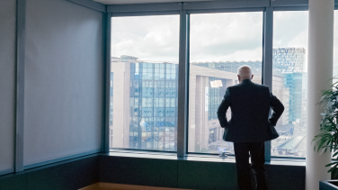 A man looks out his office window over the city.
