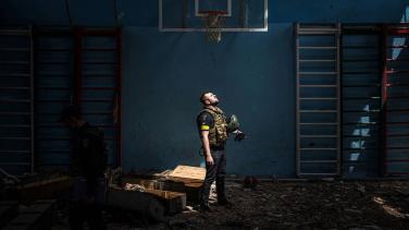 A lone Ukrainian soldier standing in a dark room looks up at a skylight.