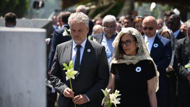 A man and a womon at a commemoration ceremony in solemn pose. 