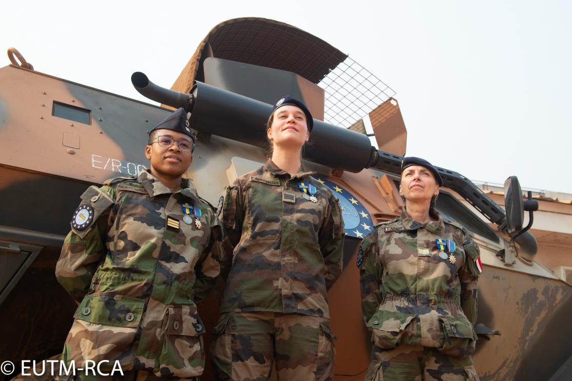 Three military women posing in front of a tank
