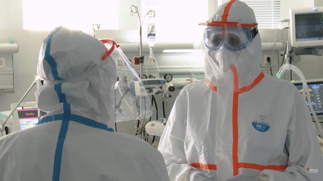 Two people in safety suits and protective shields speaking