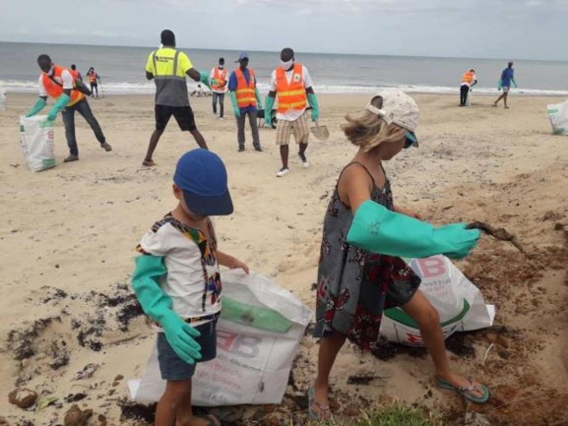 Two children cleaning the beach and throwing rubbish into bags.