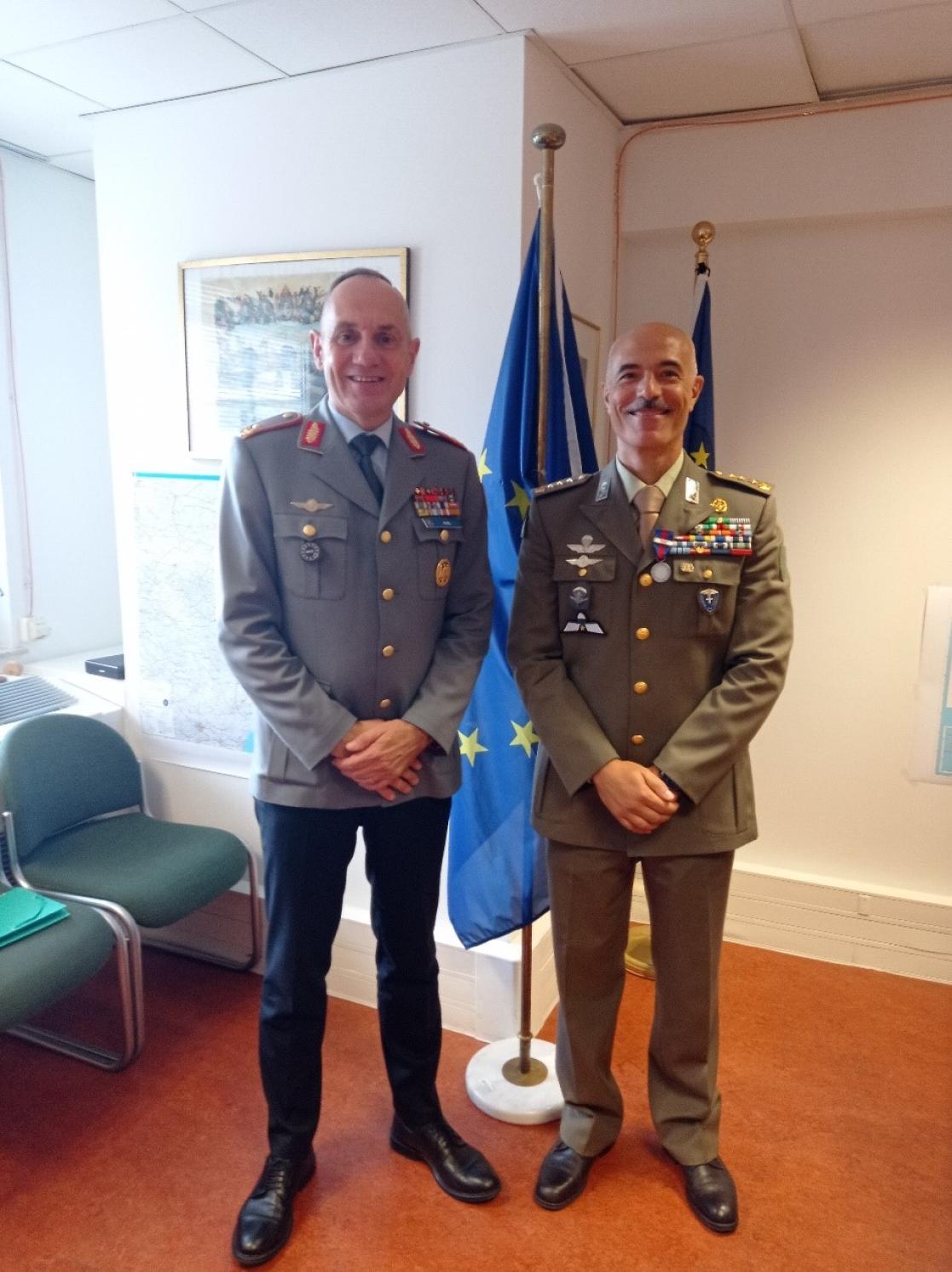 Two men in military uniform pose in front of an EU flag