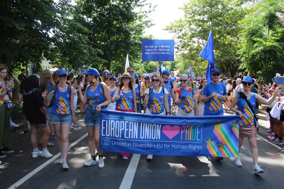 A large group of people march behind a parade sign that says "European Union Loves Pride!"