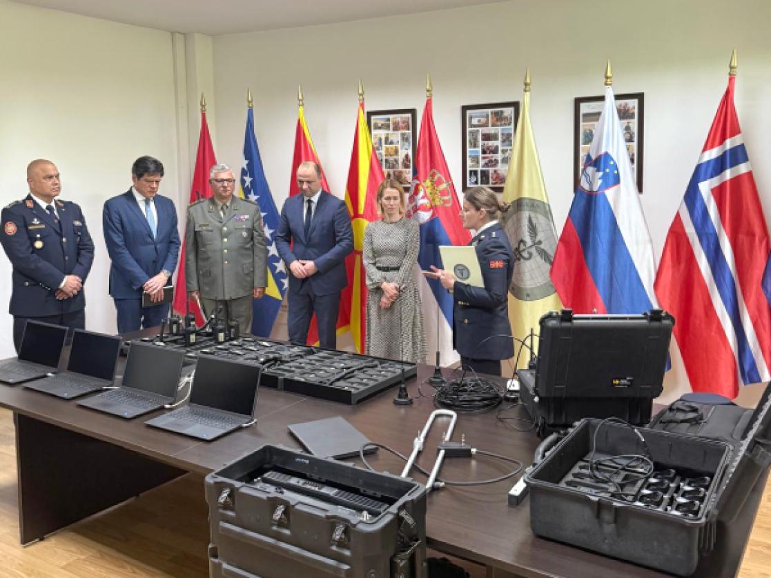In a room with flags, dignitaries, on the table is some equipment.