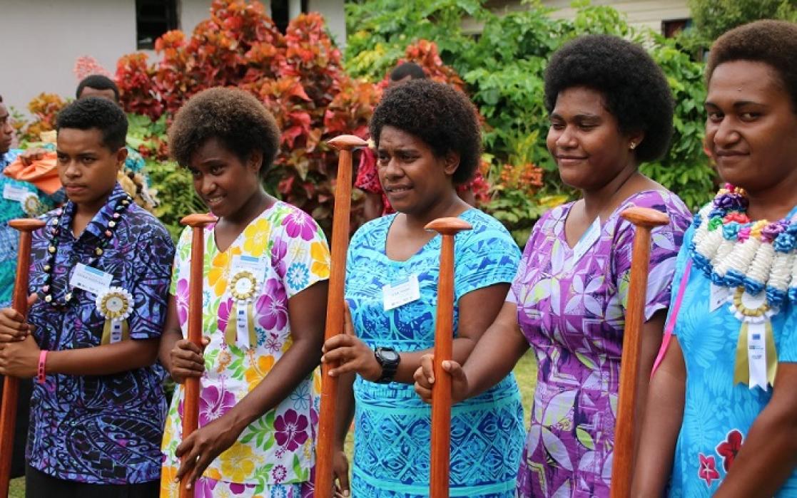  4 women and a guy in line holding a kind of stick, all of them wearing colorful clothes