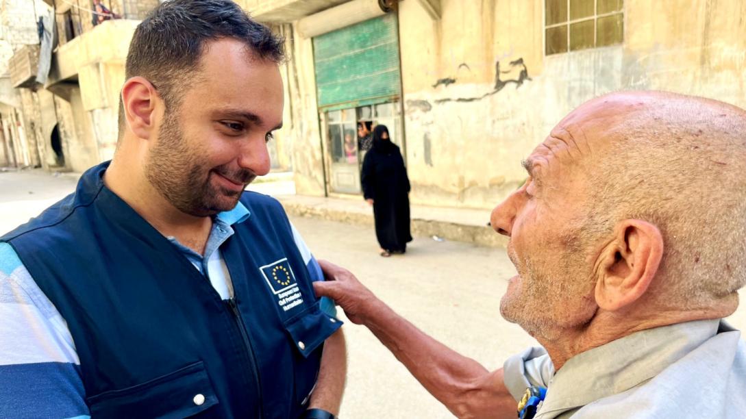 Young male EU aid worker assists older gentleman.