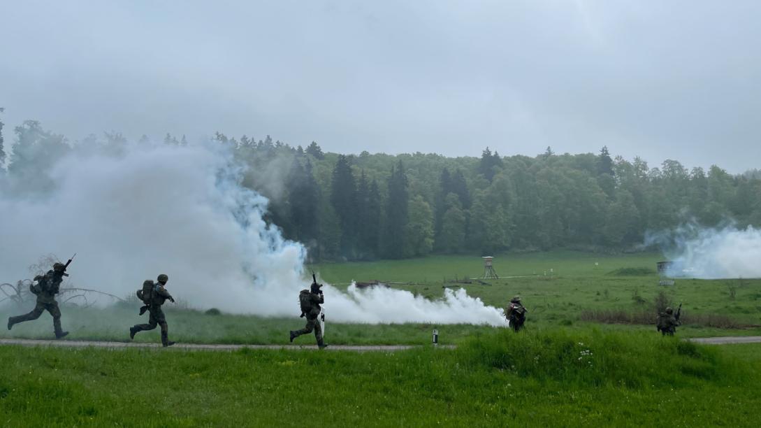 Soliders in training move across a battlefield with smoke screens
