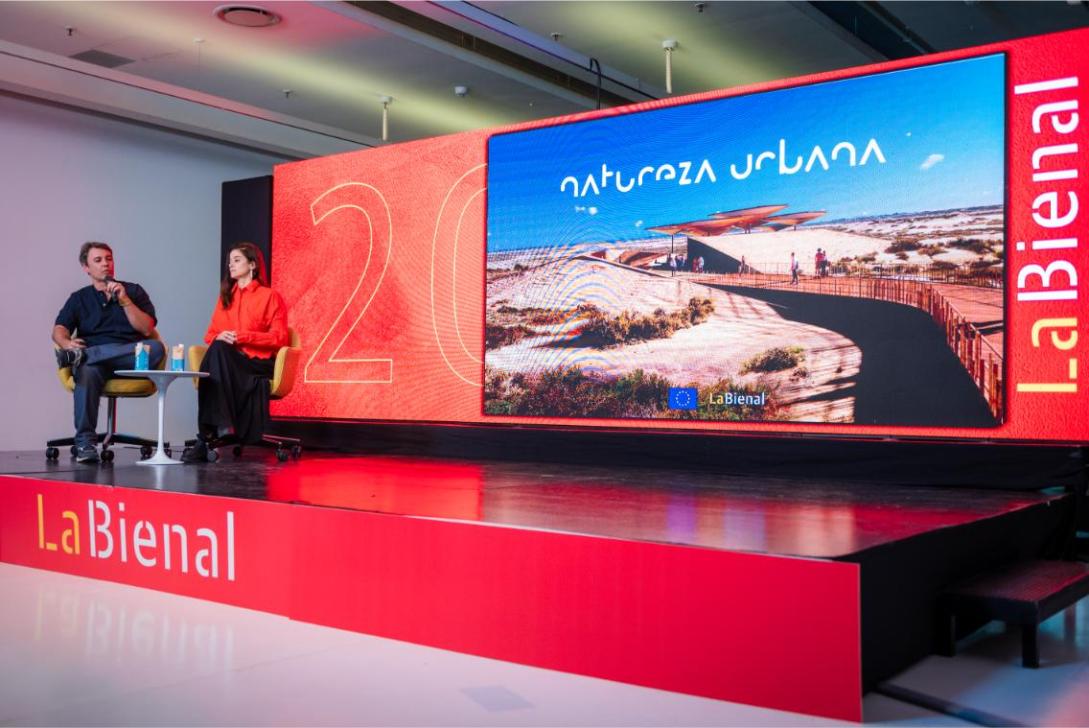 Stage at a conference with two people seated, sign says "Bienial".