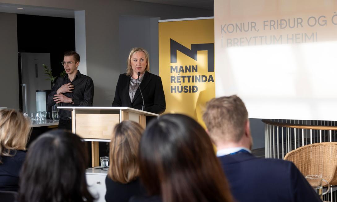 woman speaking at a podium in front of guests. A sign language interpretor to the left.