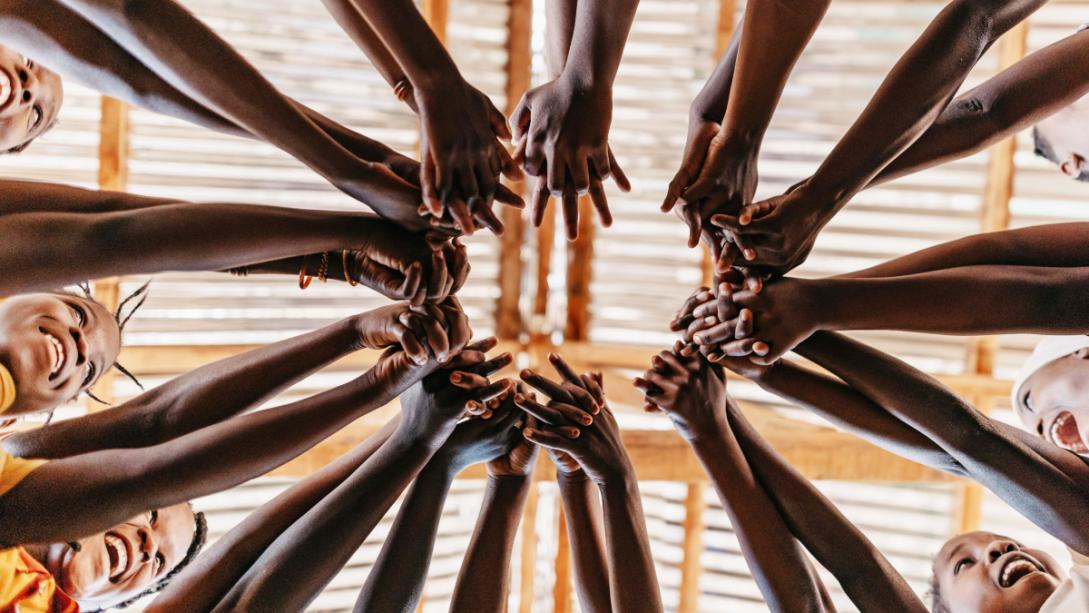 Low angle of children standing in a circle reaching out to join hands.