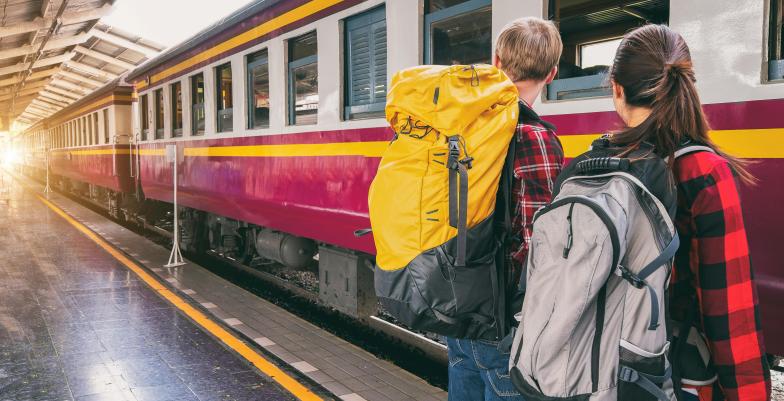 Woman and Man with backpacks waiting on Train Station in front of a train