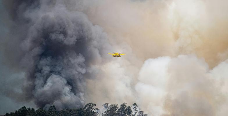 firefighting plane in the air above forest fire smoke