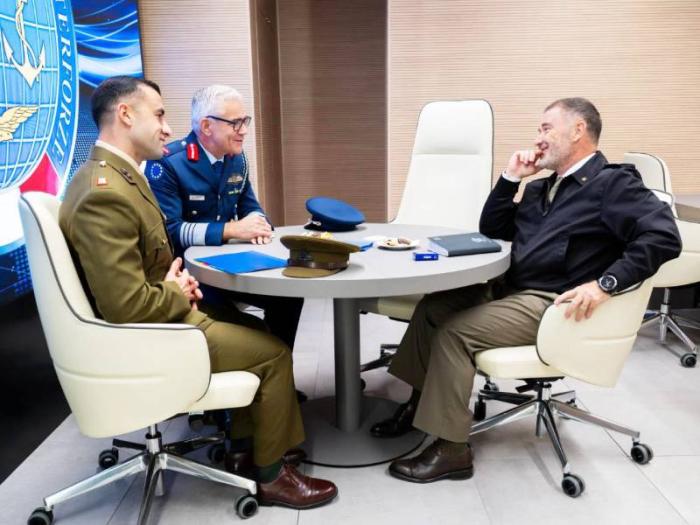 Three senior military officers sit around a table in a meeting.