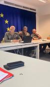 A meeting of senior military personnel in an office with a notebook in the foreground. There is an EU flag on the wall. 