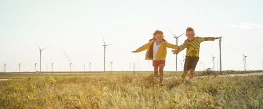 Future generations - girl and boy running in a field with wind turbines in background