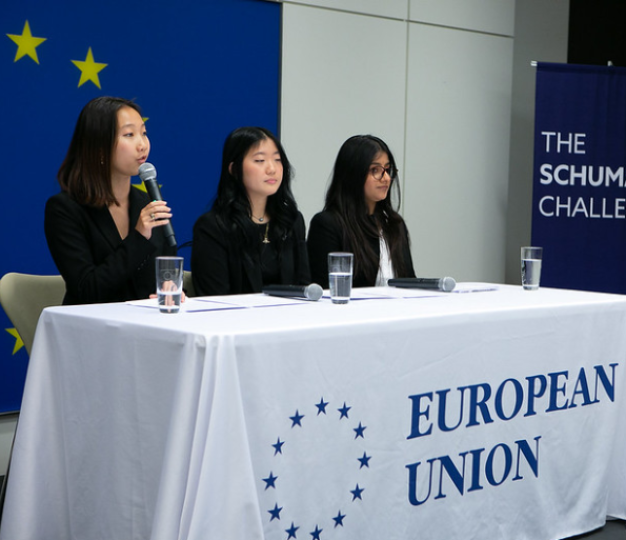 Three female students sit at a table, one speaking into a microphone.
